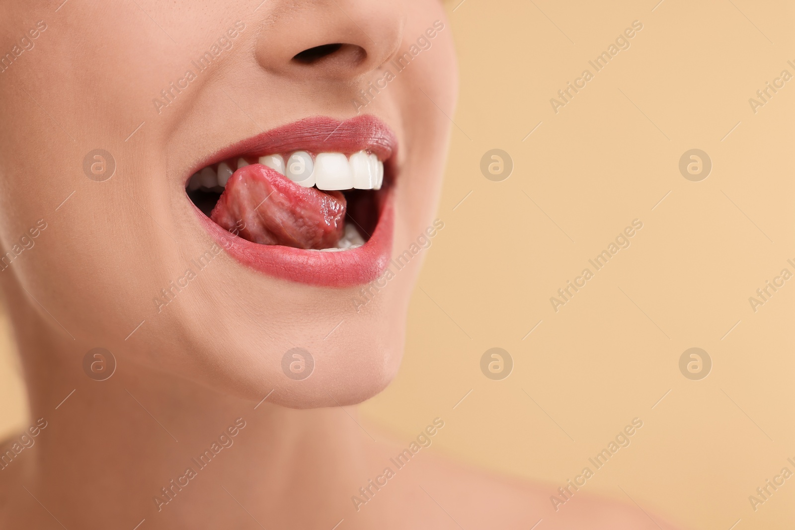 Photo of Woman with beautiful lips licking her teeth on beige background, closeup. Space for text