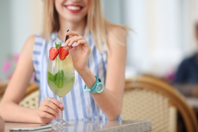 Young woman with glass of tasty lemonade in open-air cafe