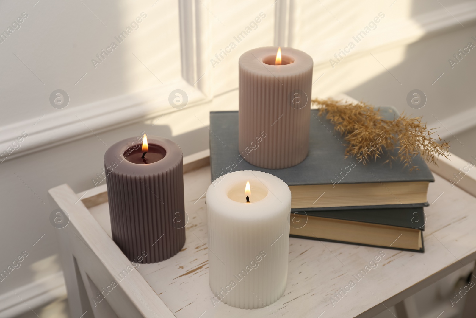 Photo of Different burning candles and books on white table indoors
