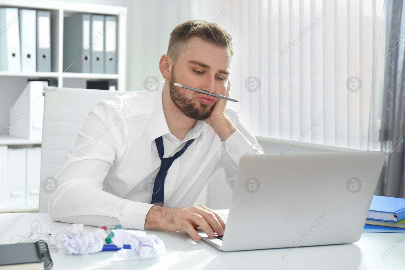 Photo of Lazy young man playing with pencil at messy table in office