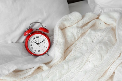 Photo of Analog alarm clock and soft blanket on bed. Time of day