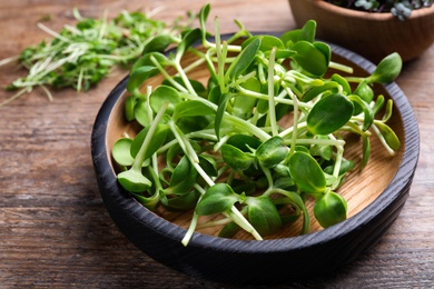 Photo of Bowl with fresh microgreen on wooden table, closeup