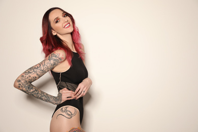 Photo of Beautiful woman with tattoos on body against light background. Space for text
