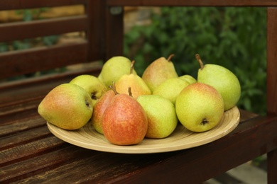 Photo of Ripe pears in wooden plate on bench in garden