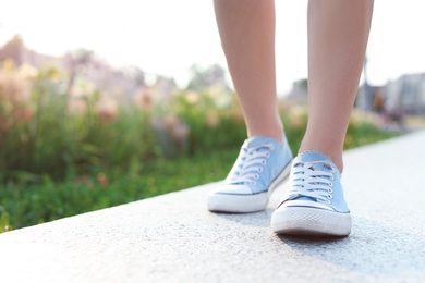 Woman in stylish sneakers walking outdoors, closeup. Urban fashion