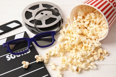 Clapper, popcorn, reel and glasses on wooden table. Cinema snack