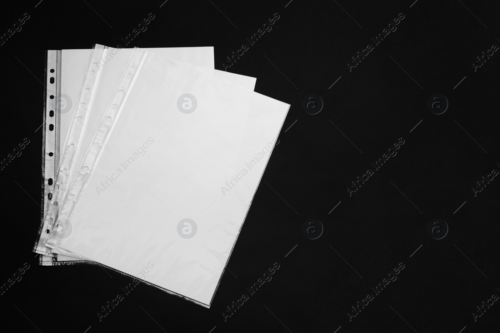 Photo of Punched pockets with paper sheets on black background, flat lay. Space for text