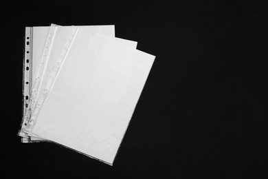 Photo of Punched pockets with paper sheets on black background, flat lay. Space for text