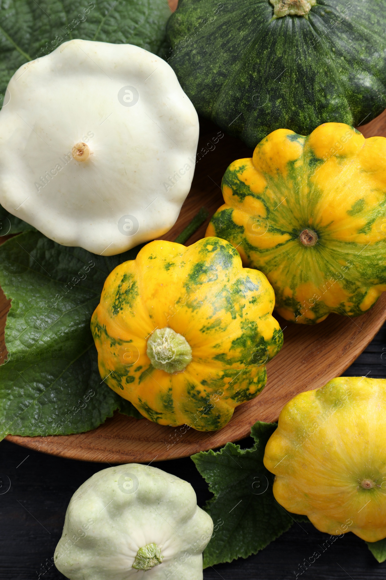 Photo of Fresh ripe pattypan squashes with leaves on black  table, flat lay