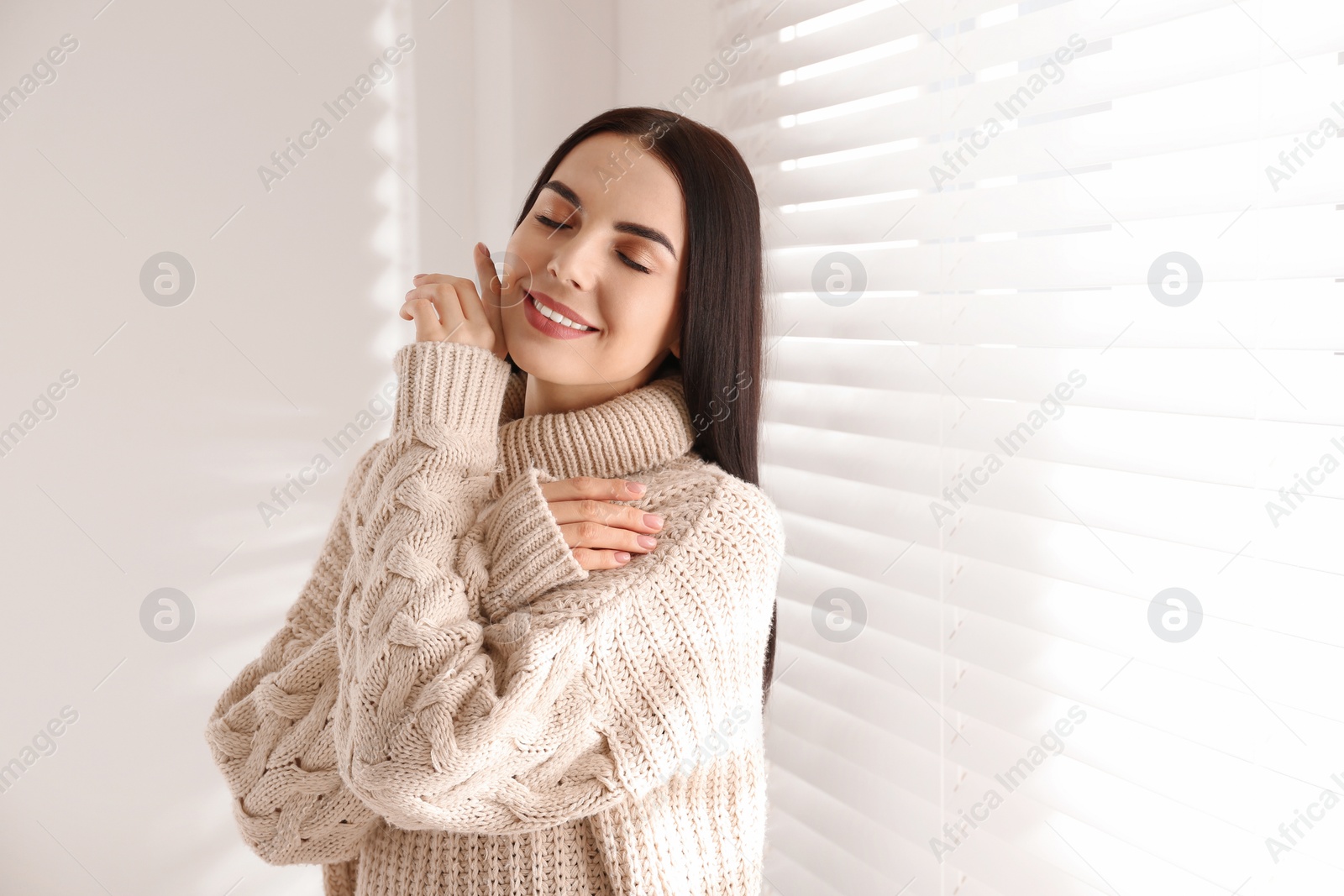 Photo of Young woman wearing warm sweater near window at home. Winter season