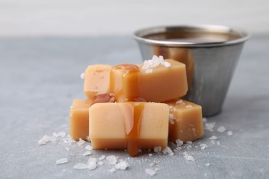 Yummy caramel candies, sauce and sea salt on grey table, closeup