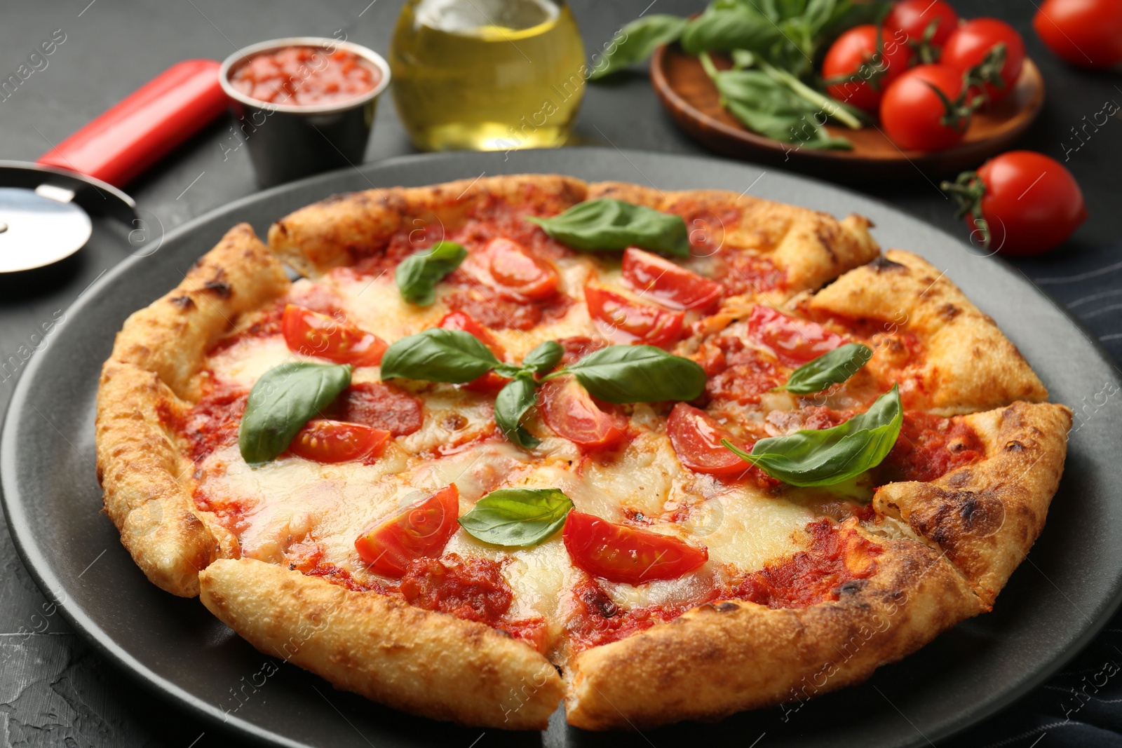 Photo of Delicious Margherita pizza, ingredients and cutter on black table, closeup