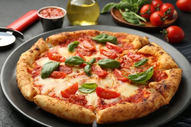 Photo of Delicious Margherita pizza, ingredients and cutter on black table, closeup