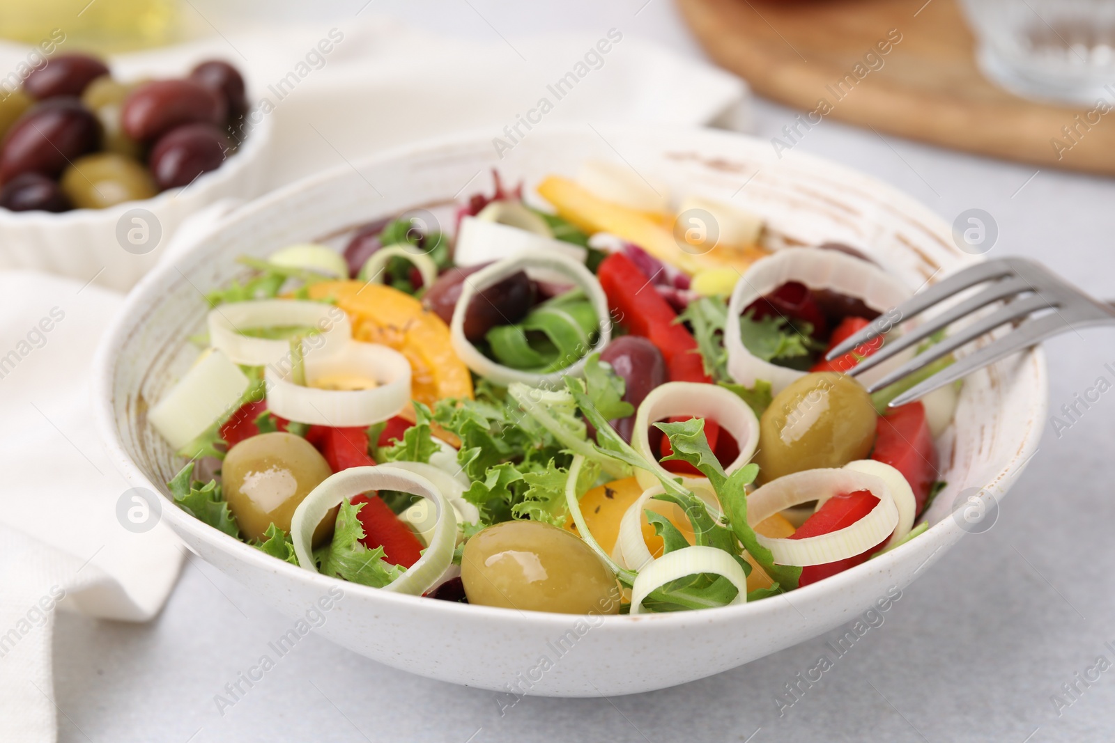 Photo of Bowl of tasty salad with leek and olives on light table, closeup