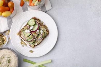 Tasty vegan sandwich with cucumber, onion, hummus and pumpkin seeds on light grey table, flat lay. Space for text