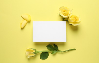 Beautiful roses, petals and blank card on yellow background, flat lay. Space for text