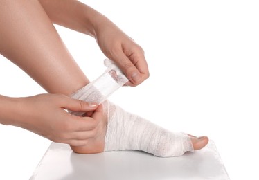 Photo of Woman wrapping foot in medical bandage on white background, closeup