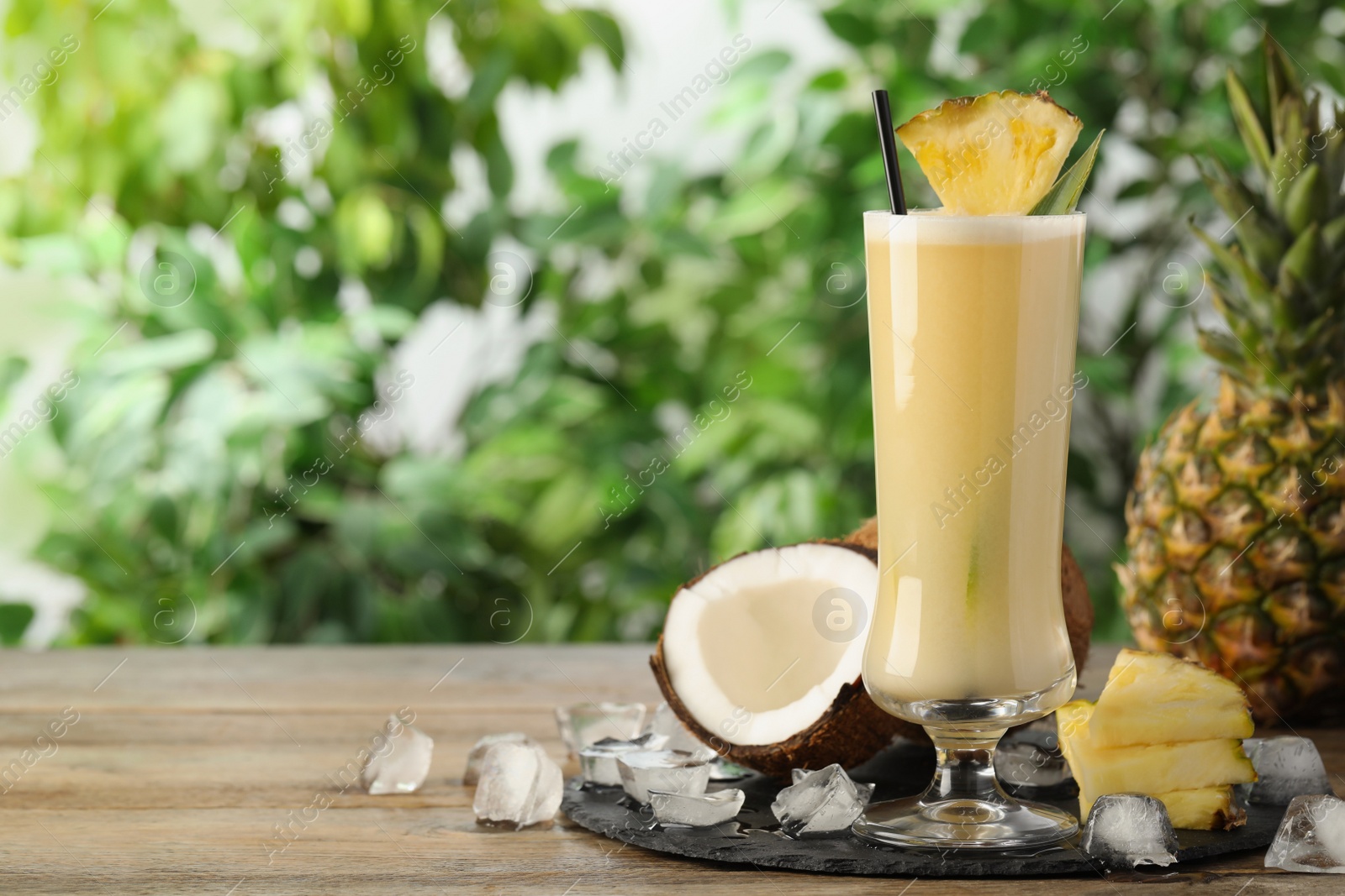 Photo of Tasty Pina Colada cocktail and ingredients on wooden table, space for text