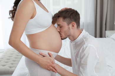 Photo of Young husband kissing his pregnant wife's tummy in bedroom