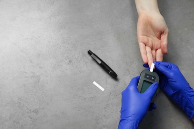 Diabetes. Doctor checking patient's blood sugar level with glucometer at gray table, top view. Space for text