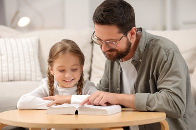 Photo of Girl and her godparent reading Bible together at table in room