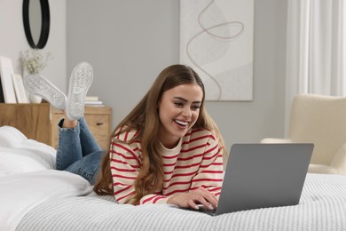 Happy woman with laptop on bed in bedroom
