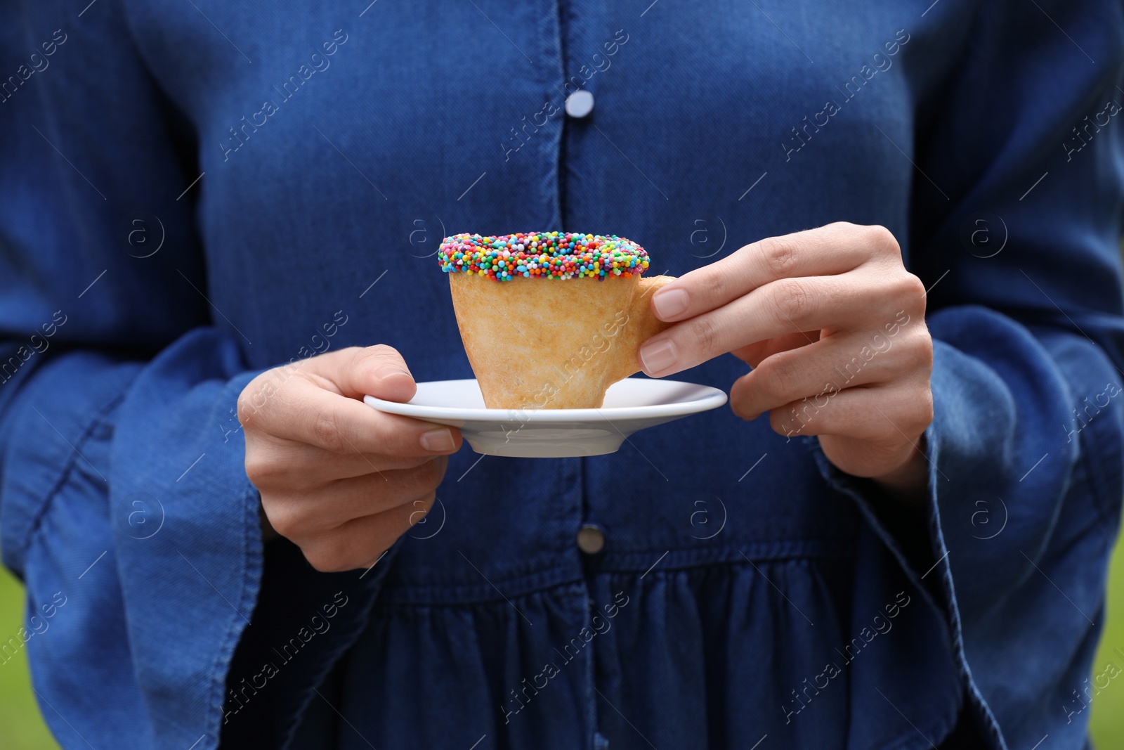 Photo of Woman holding delicious edible biscuit cup of coffee decorated with sprinkles outdoors, closeup