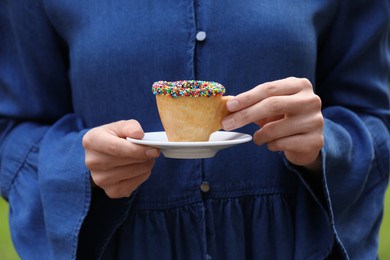 Photo of Woman holding delicious edible biscuit cup of coffee decorated with sprinkles outdoors, closeup