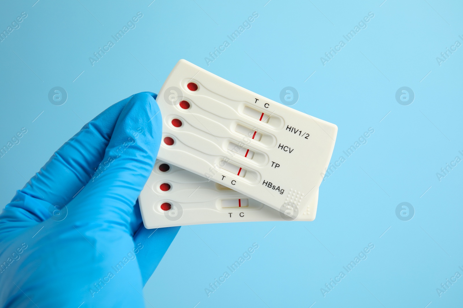 Photo of Doctor holding two disposable express tests for hepatitis on light blue background, closeup