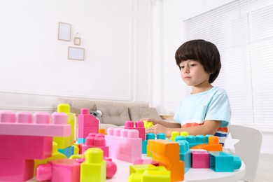 Photo of Cute little boy playing with colorful building blocks at table in living room