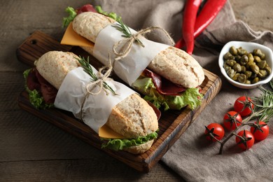 Photo of Delicious sandwiches with bresaola, lettuce and other products on wooden table