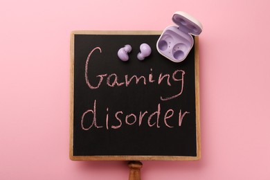 Photo of Small chalkboard with written phrase Gaming Disorder and earphones on pink background, top view
