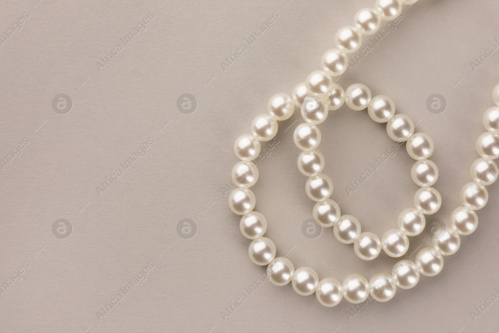 Photo of Elegant pearl necklace on beige background, top view. Space for text