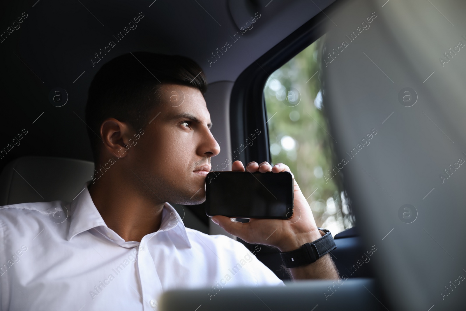 Photo of Handsome man with smartphone on backseat of modern car