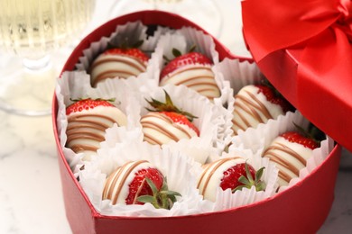 Photo of Heart shaped box with delicious chocolate covered strawberries on white marble table, closeup