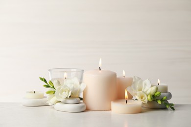 Beautiful composition with burning candles, spa stones and flowers on white table. Space for text