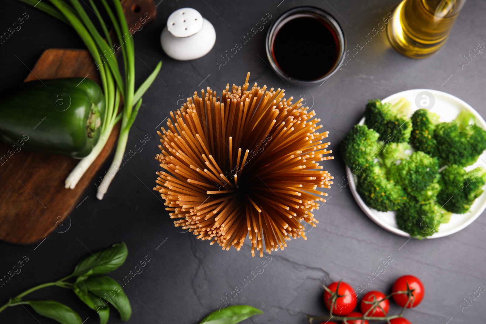 Photo of Uncooked buckwheat noodles and fresh ingredients on black table, flat lay