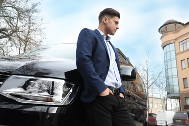 Handsome man near modern car outdoors, low angle view