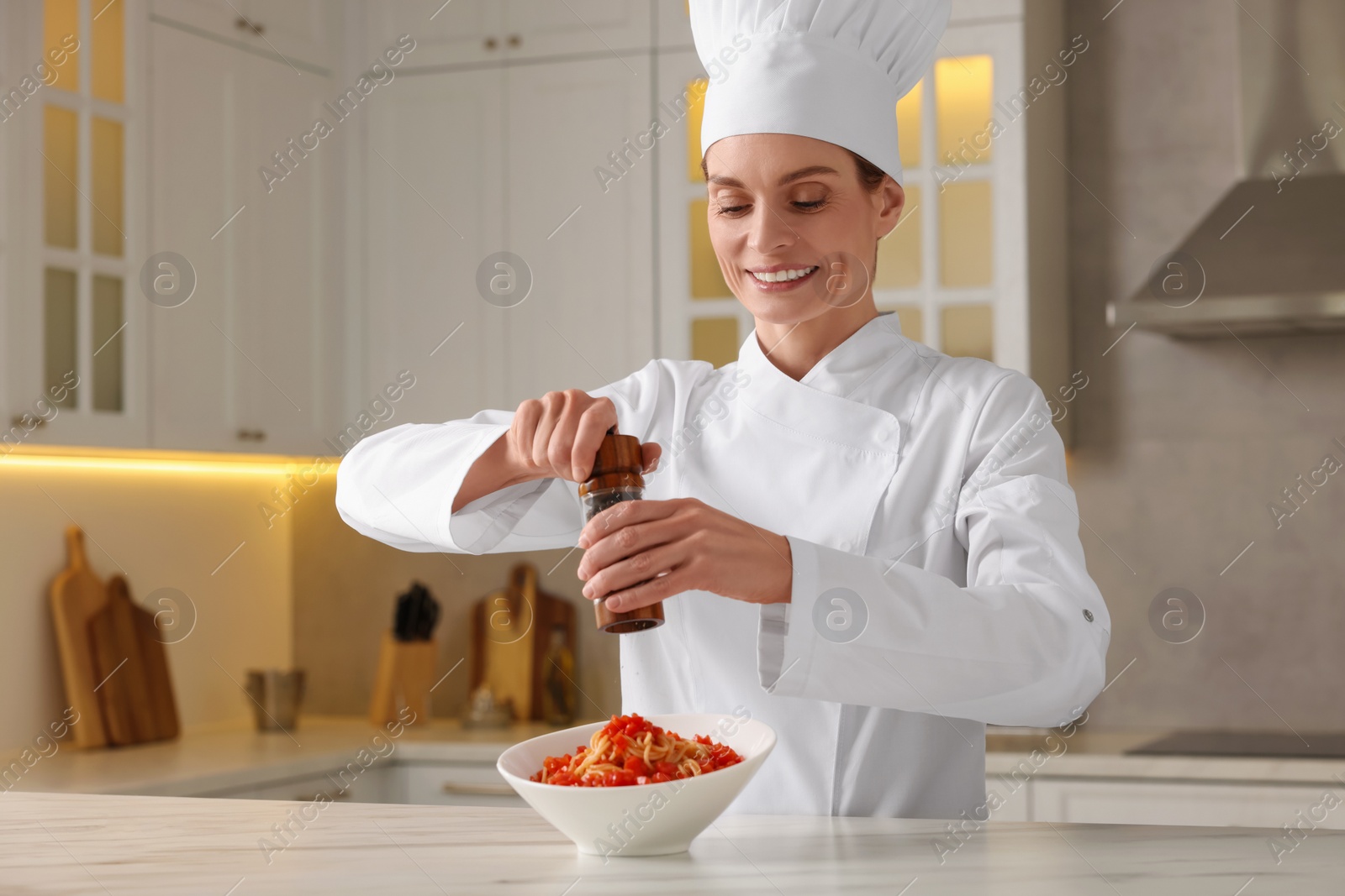 Photo of Professional chef adding pepper into delicious dish at white marble table in kitchen