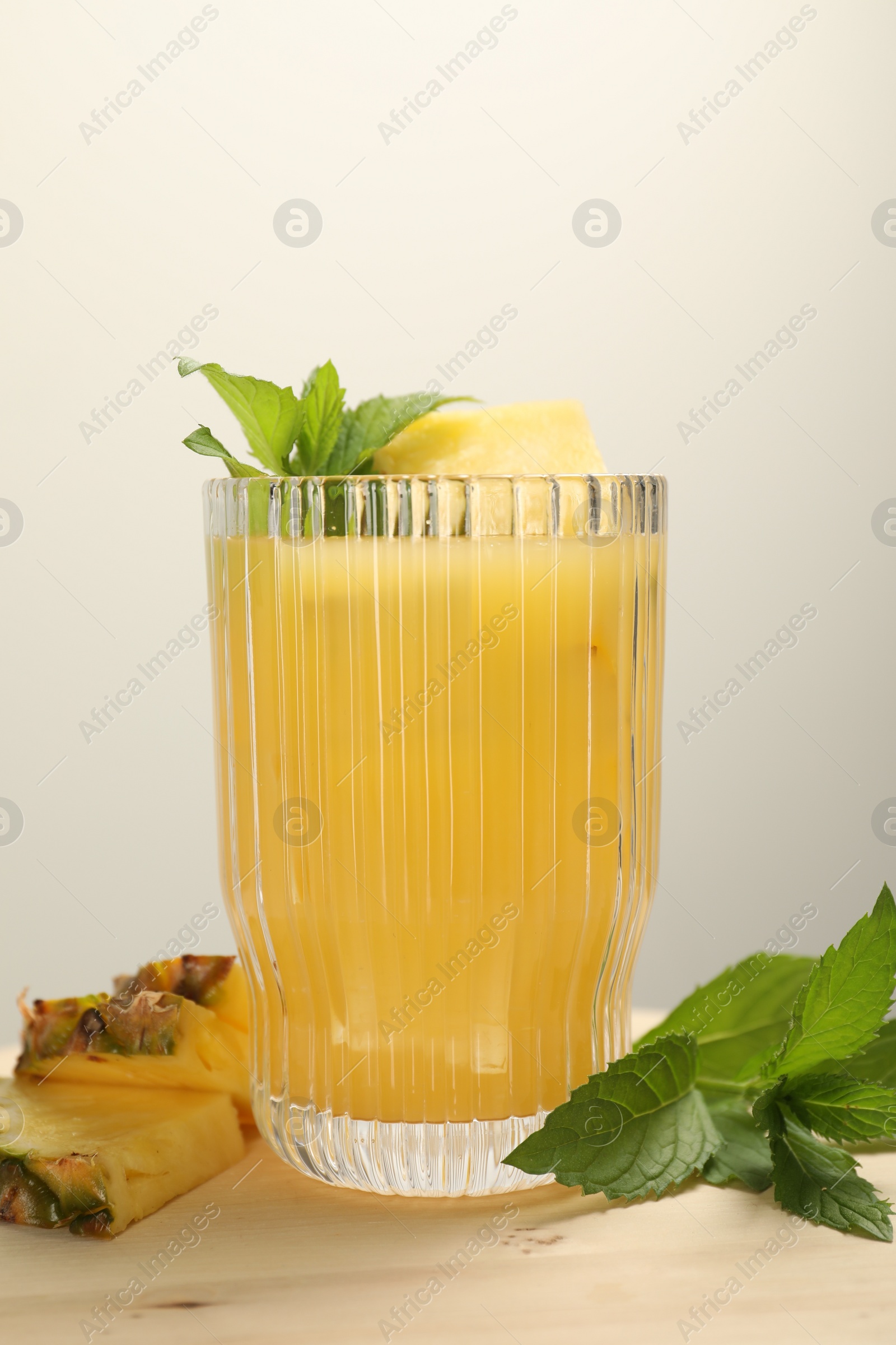 Photo of Glass of tasty pineapple cocktail, mint and sliced fruit on wooden board, closeup