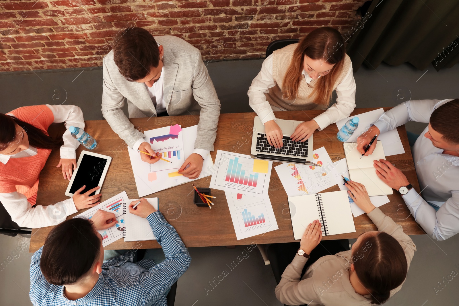 Photo of Team of employees working together at wooden table in office, above view