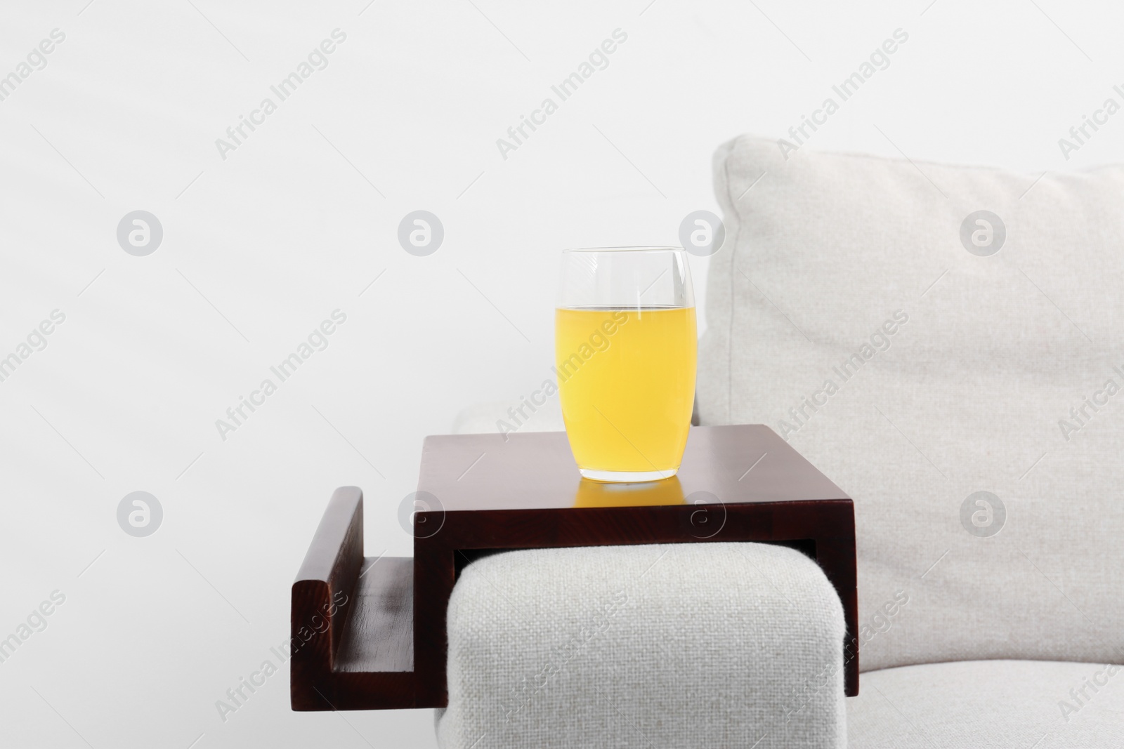 Photo of Glass of juice on sofa with wooden armrest table indoors. Interior element