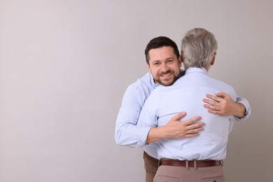 Happy son and his dad hugging on gray background, space for text