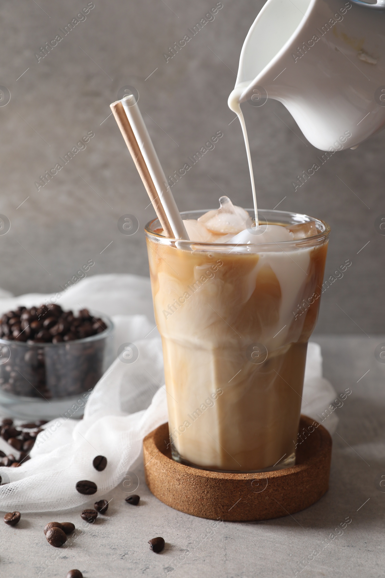 Photo of Pouring milk into glass with refreshing iced coffee at gray table, closeup