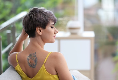 Trendy young woman with tattoo on sofa indoors