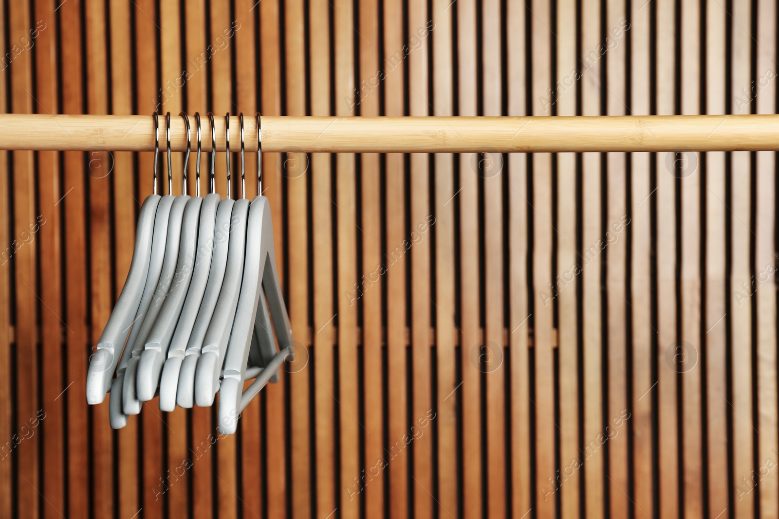 Photo of Empty hangers on rail against wooden background, space for text