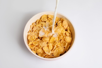 Photo of Milk pouring into bowl with crispy cornflakes on white background