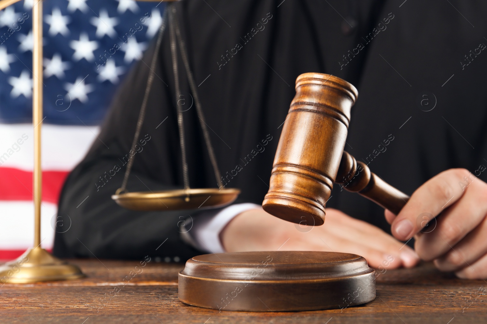 Photo of Judge with gavel at wooden table near flag of United States, closeup