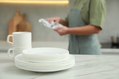 Photo of Woman wiping dish with towel in kitchen, focus on stack of plates