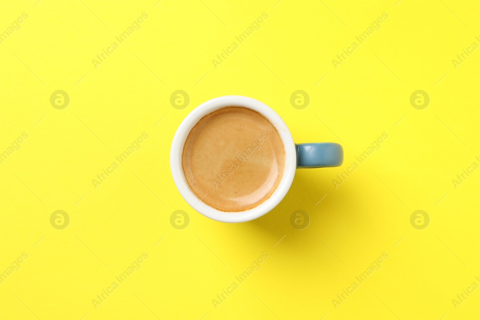 Photo of Aromatic coffee in cup on yellow background, top view